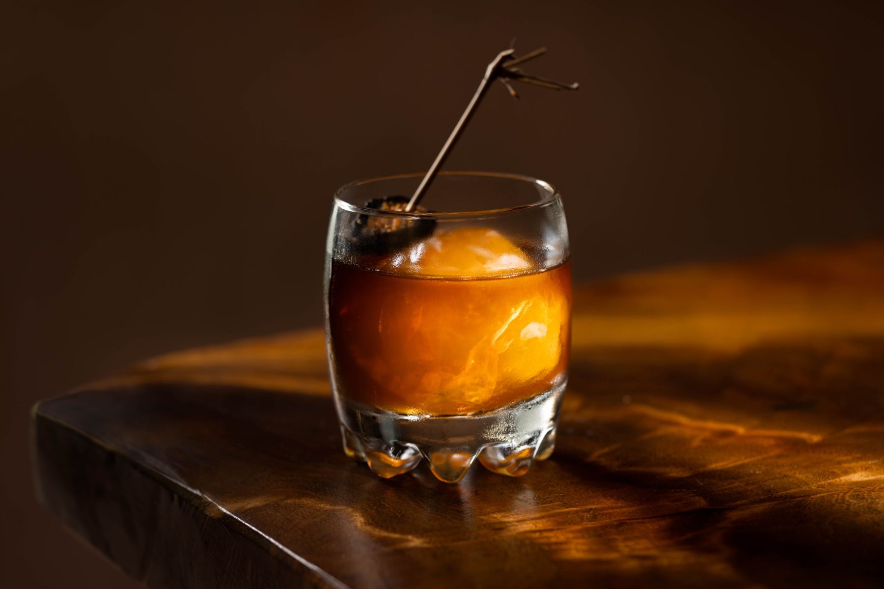 Amber stirred drink over a clear ice sphere