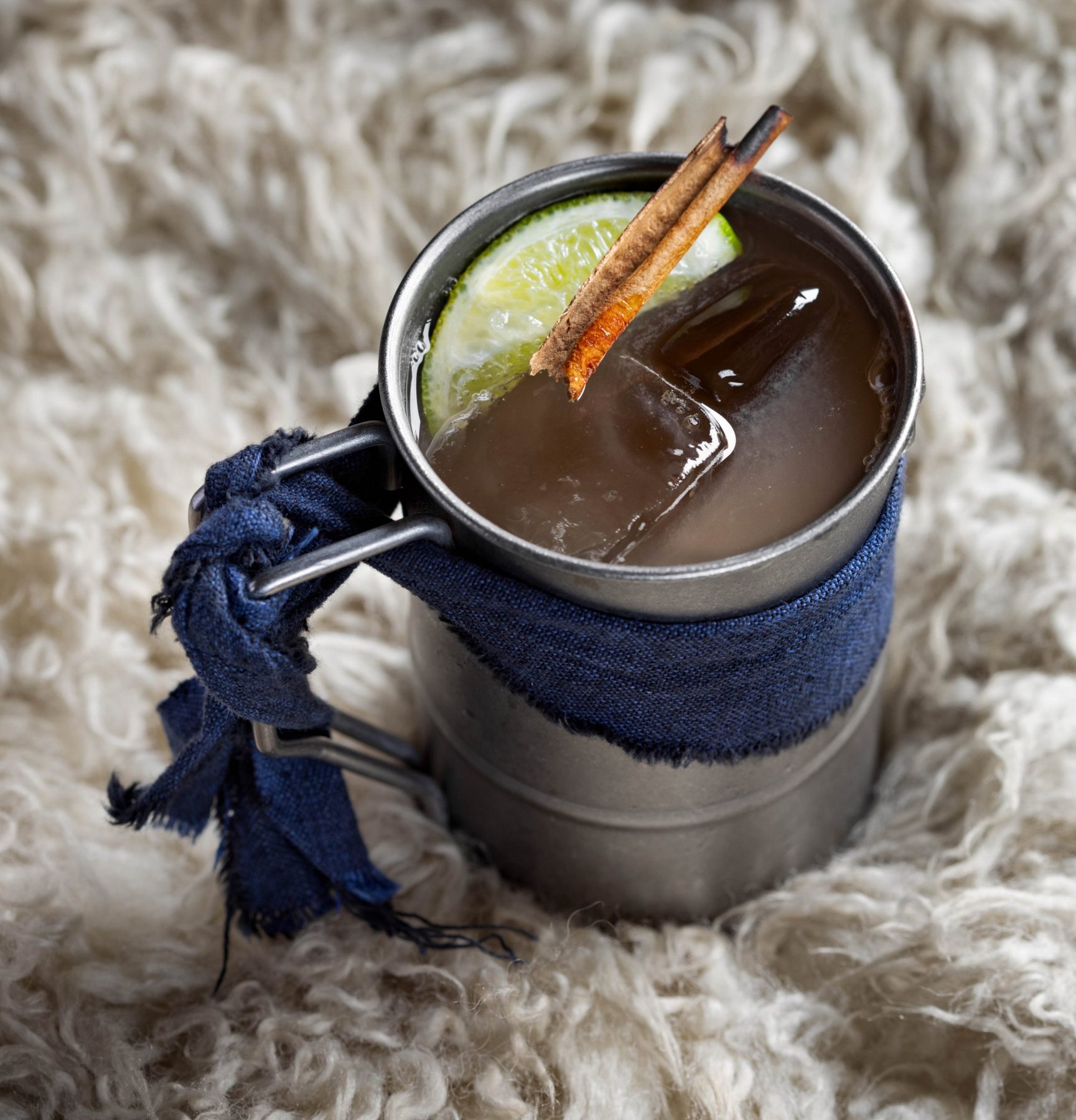 Tin cup cocktail with lime and charred cinnamon on sheepskin