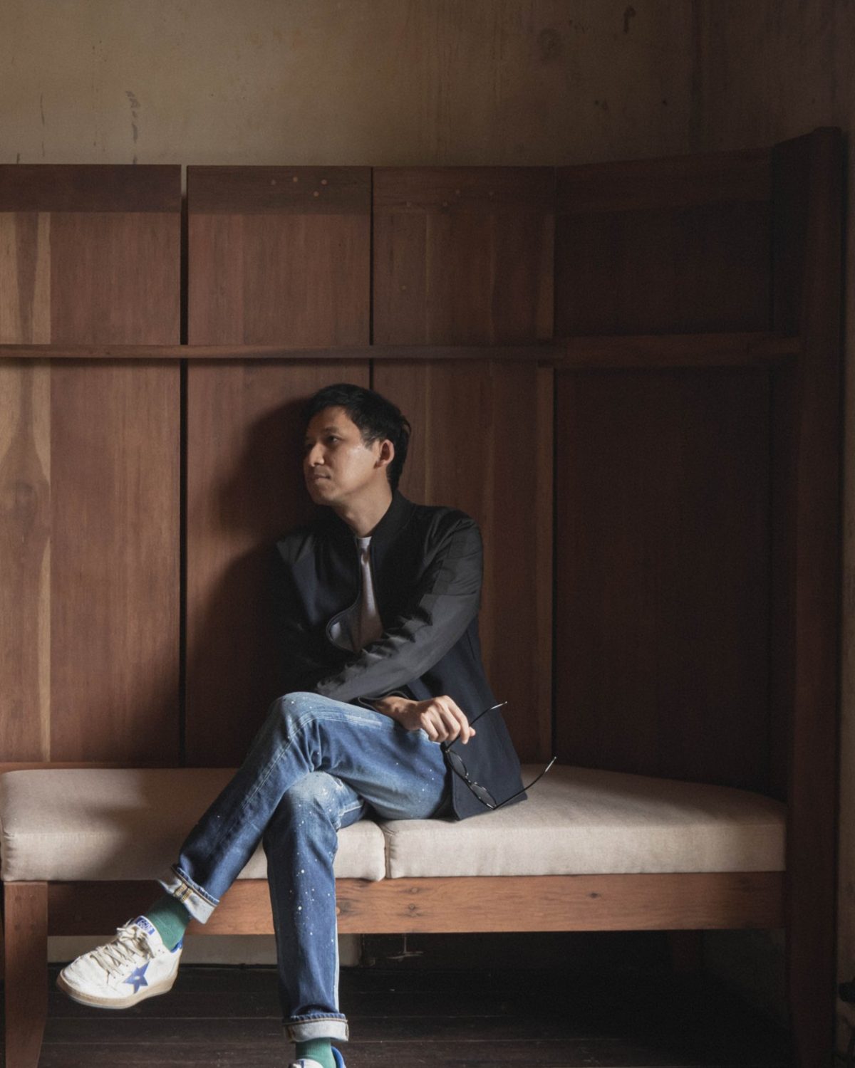 Tao seated on the teak banquette under a pendant lamp